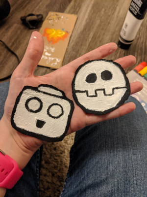 me holding two patches I made, one is a serv bot head and the other is the bonne family emblem a circular robotic looking skull