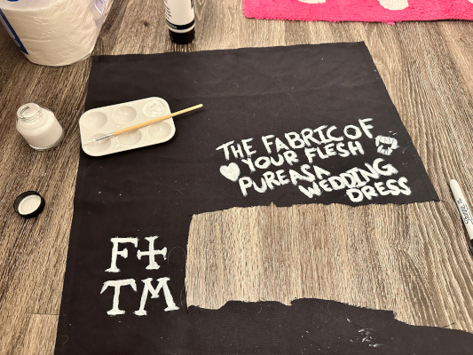 a black cloth with two patches: one says F+TM for Florence and the Machine, the other says The fabric of your flesh pure as a wedding dress with fangs