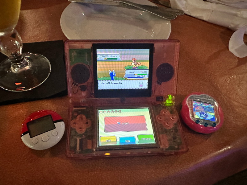 a clear pink ds lite between a pokewalker and tamagothci