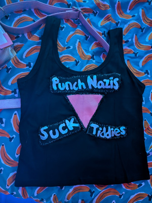 a black crop top that says "punch nazis suck tiddies" with a pink triangle in the middle