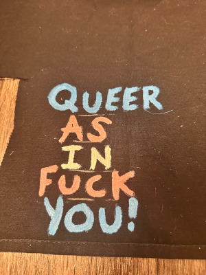 the text Queer as in Fuck You! in trans colors alternating per word